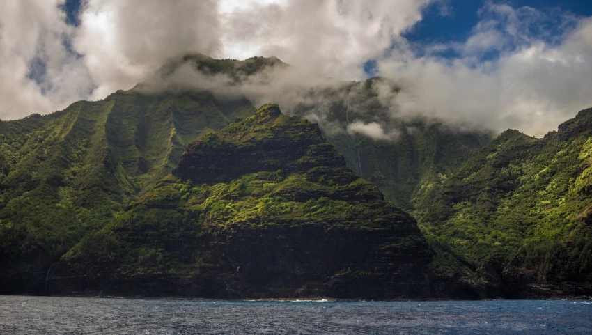 a body of water with a mountain in the background, a picture, by Adam Manyoki, unsplash, plein air, polynesian style, steep cliffs, covered in clouds, tim hildebrant