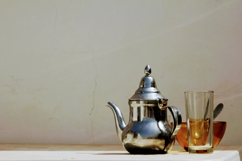 a silver tea pot sitting next to a glass of tea, by Youssef Howayek, pexels, photorealism, tuareg, afternoon sun, old picture, minimalism