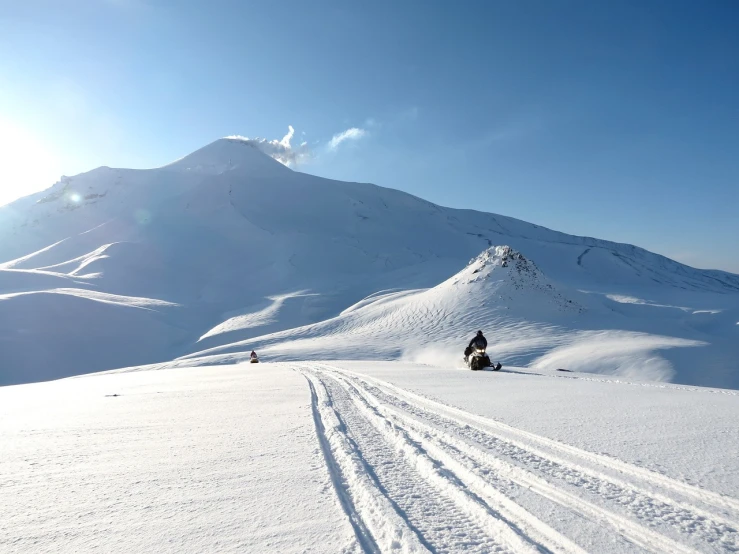 a person riding skis down a snow covered slope, by Andrei Kolkoutine, volcano in background, georgic, beautiful environment, reportage photo