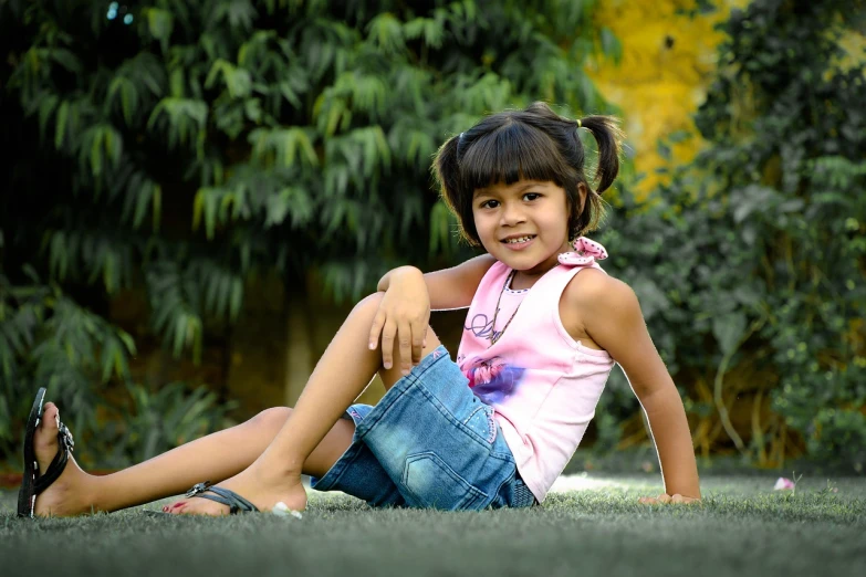 a little girl that is sitting in the grass, a picture, by Basuki Abdullah, pixabay, realism, wearing a camisole and shorts, assamese, (beautiful) girl, with a cool pose