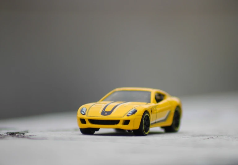 a yellow toy car sitting on top of a white surface, a tilt shift photo, inspired by Bernardo Cavallino, unsplash, hq 4k phone wallpaper, a tvr sagaris, yellow and black trim, 4 k vertical wallpaper