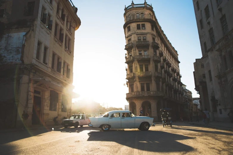 a white car driving down a street next to tall buildings, by Youssef Howayek, golden hour sunlight, cuban revolution, light above palace, cars parked underneath