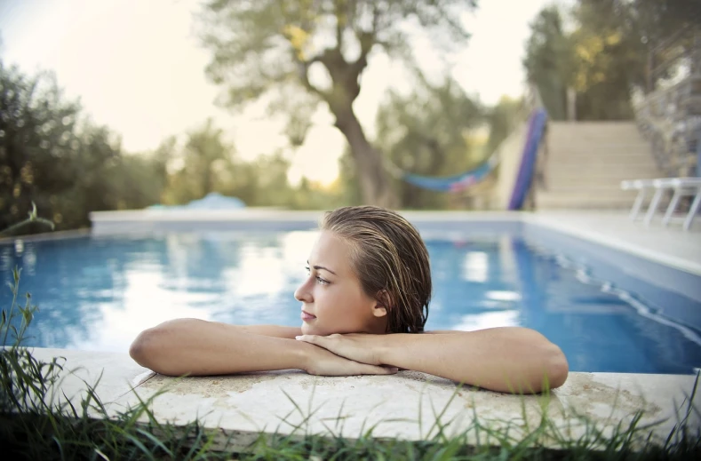 a woman sitting at the edge of a swimming pool, a portrait, by Julian Allen, pexels, smooth in _ the background, small wellness relaxation pool, peaceful face, nature outside