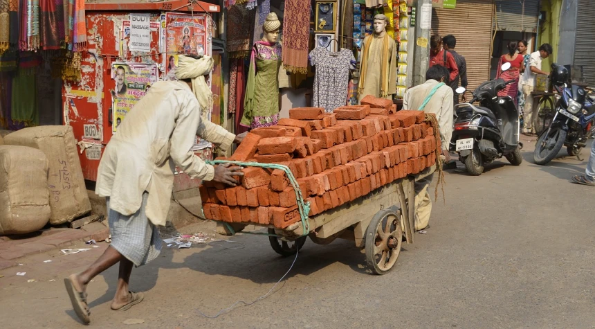 a man pushing a cart full of bricks down a street, flickr, hindu, red sandstone natural sculptures, people at work, built on a small