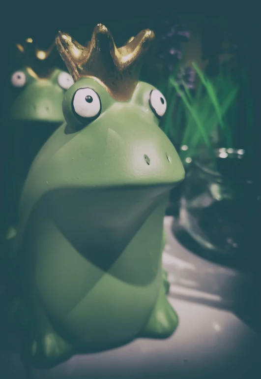 a green frog with a golden crown on its head, a picture, inspired by Jeff Koons, unsplash, retro effect, happy meal toy, they are watching, animal - shaped cake