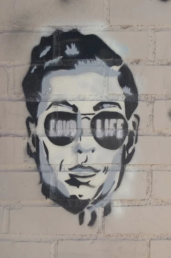 a painting of a man with sunglasses on a brick wall, graffiti art, inspired by John Cale, life is not what it used to be, close-up photo, adrien brody, life like
