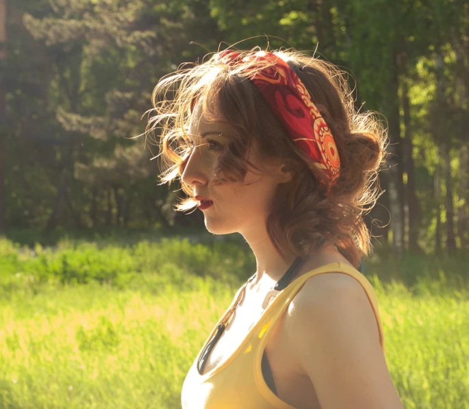 a woman standing on top of a lush green field, by Pamela Ascherson, flickr, romanticism, colorful bandana, ginger wavy hair, side profile shot, yellow and red