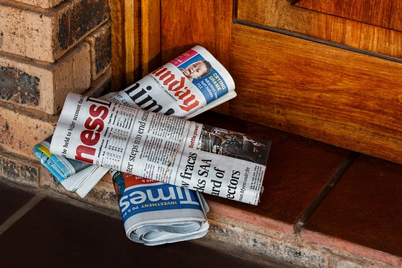 a pile of newspapers on the ground next to a door, a picture, by John Murdoch, unsplash, miscellaneous objects, tim hildebrant, advertisement, half image