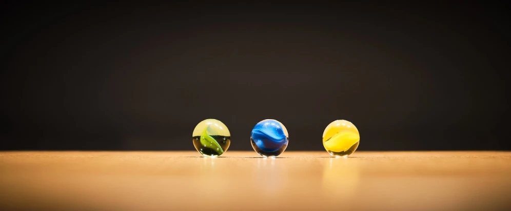 three marbles sitting on top of a wooden table, by Jan Rustem, unsplash, hyperrealism, some yellow green and blue, profile pic, miniature product photo, inside a marble