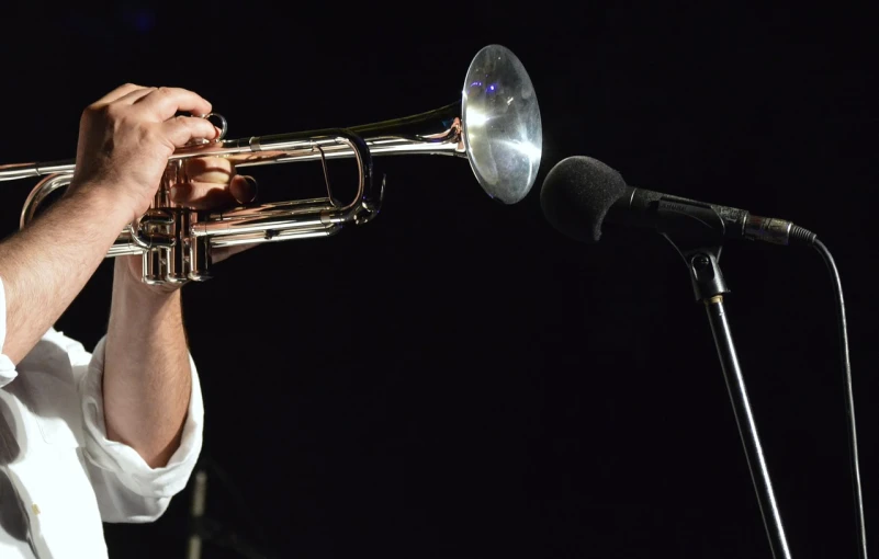 a man playing a trumpet in front of a microphone, pixabay, afp, bottom angle, photograph credit: ap, jeremy bennett