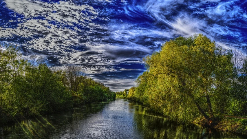 a river running through a lush green forest, by Antoni Brodowski, flickr, colorful dramatic puffy clouds, hannover, deep blue sky, willow trees