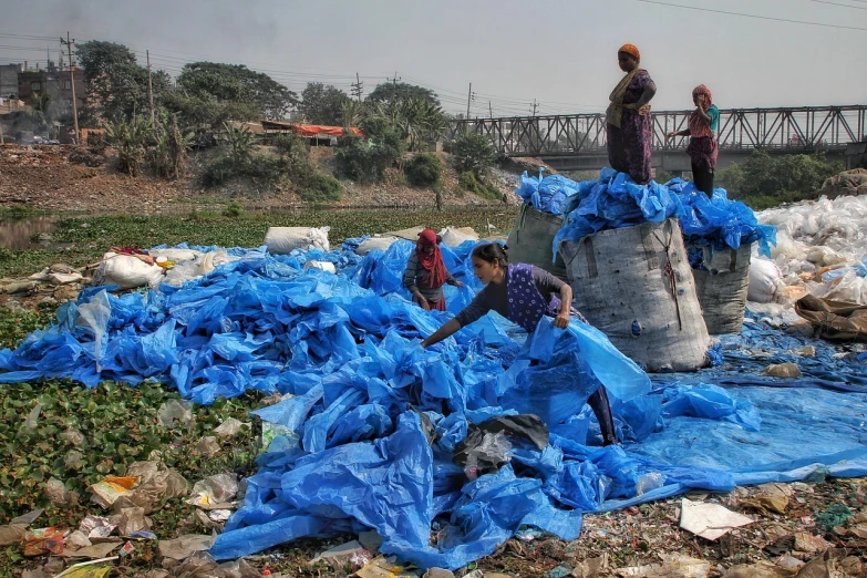 a group of people standing on top of a pile of trash, a picture, flickr, plasticien, dhaka traffic, wearing a plastic blue dress, bioremediation, bag