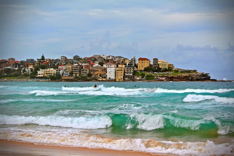 a man riding a surfboard on top of a wave in the ocean, a tilt shift photo, by Peter Churcher, art nouveau, bondi beach in the background, waterfront houses, sables crossed in background, villa