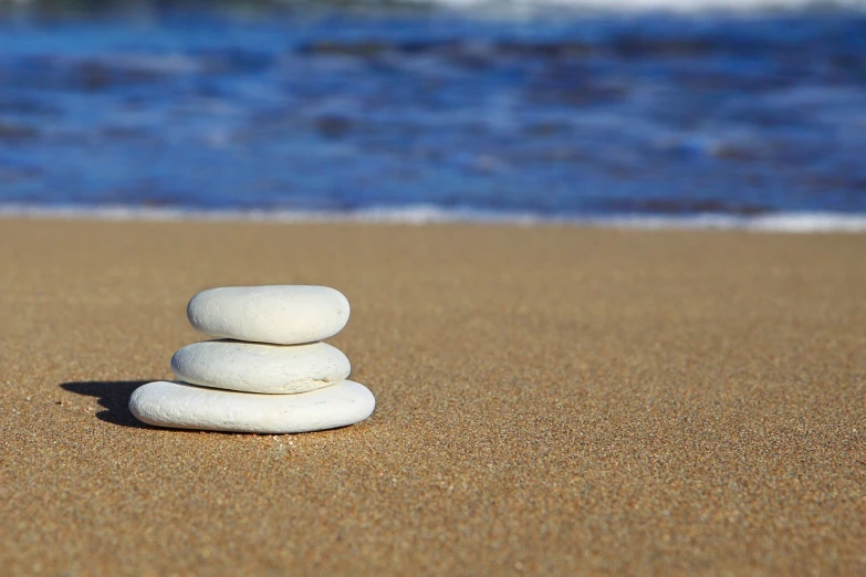 a stack of rocks sitting on top of a sandy beach, simplified, white beaches, stepping stones, laying on a beach