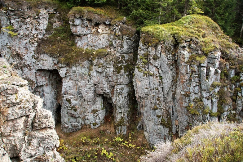 a man standing on top of a cliff next to a forest, by Hans Fischer, flickr, les nabis, overgrown stone cave, depth detail, alaska, jagged metal landscape