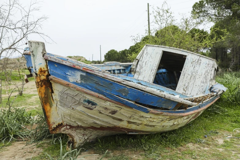 a blue and white boat sitting on top of a grass covered field, a picture, by Richard Carline, pixabay, auto-destructive art, photo of poor condition, side view close up of a gaunt, wooden boat, 3 / 4 wide shot