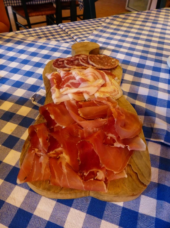 a wooden cutting board topped with meat on top of a blue and white checkered table cloth, by Antonio Saura, salami, in the dolomites, very silly looking, ham
