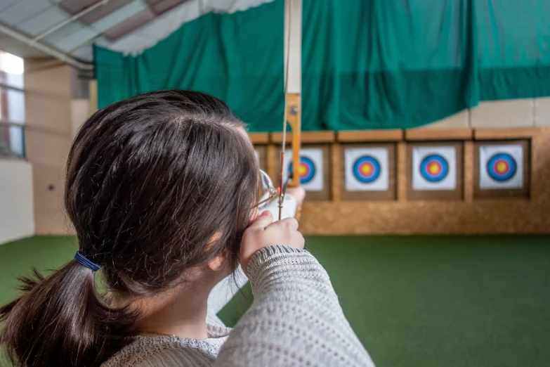 a woman holding a bow and aiming at a target, a picture, indoor shot, kids, head and shoulder shot, avatar image