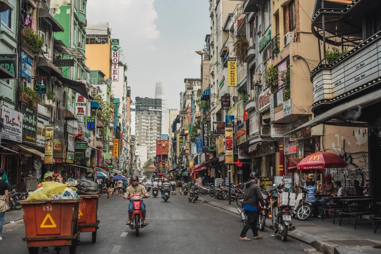 a group of people riding motorcycles down a street, a photo, by Richard Carline, shutterstock, wet market street, the neat and dense buildings, 33mm photo, scale of a city