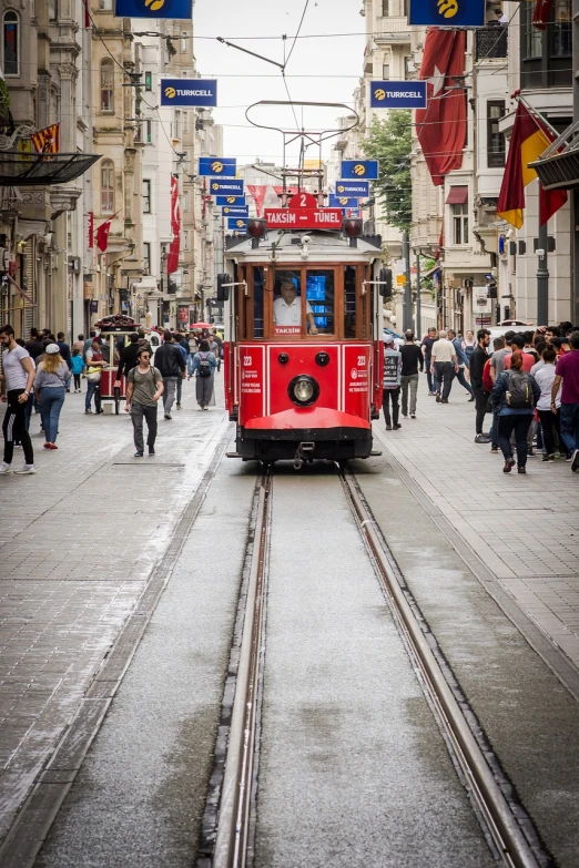 a red trolley traveling down a street next to tall buildings, a tilt shift photo, by Niyazi Selimoglu, art nouveau, ottoman empire era, very known photo, selfie photo, high resolution photo