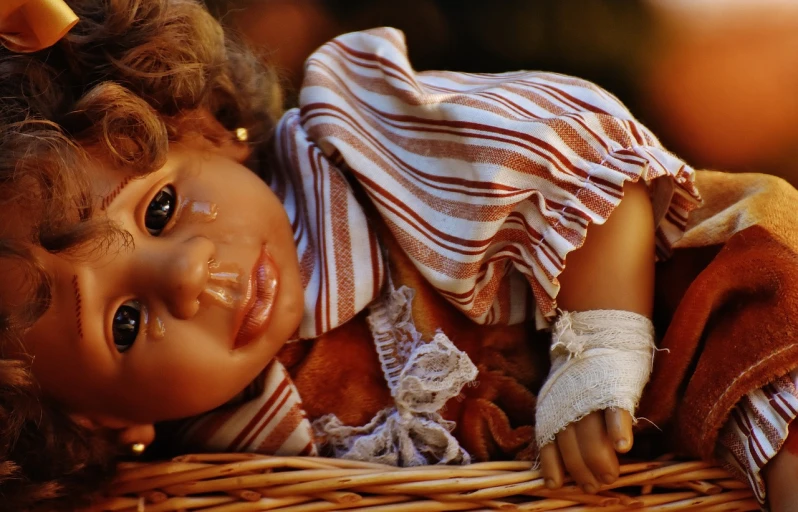 a close up of a doll in a basket, a picture, trending on pixabay, renaissance, injured, stripes, warm glow, childish look