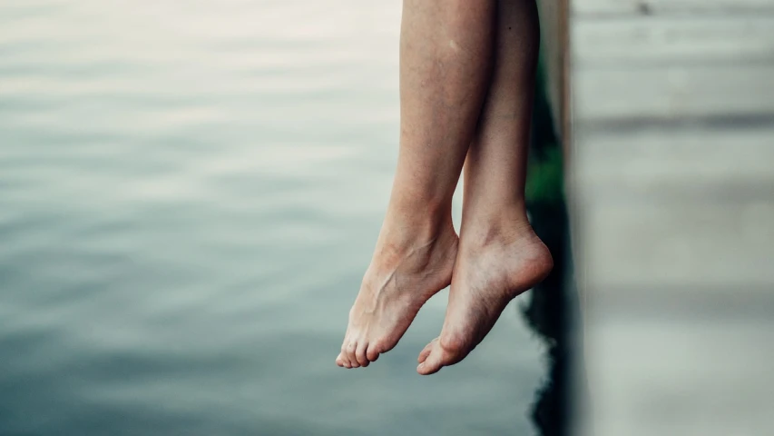 a close up of a person's legs near a body of water, floating in the air, warts, jump, hanging veins