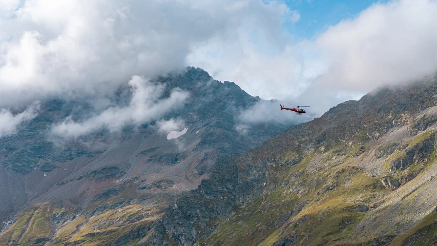 a helicopter flying over a mountain on a cloudy day, by Werner Andermatt, 2 0 2 2 photo, tourist photo, avangard, cinnabar