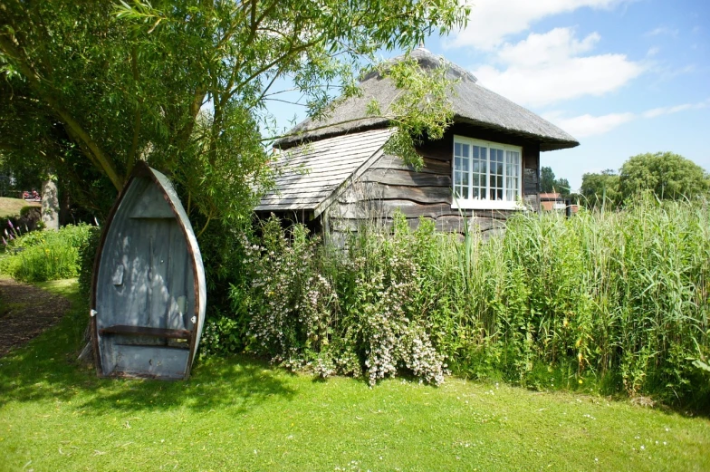 a boat sitting on top of a lush green field, a picture, by Edward Clark, shutterstock, arts and crafts movement, shed, seen from outside, walton ford, witch hut