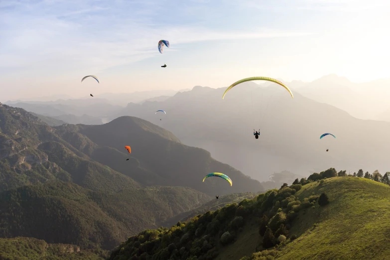 a group of people flying kites over a lush green hillside, a picture, by Cedric Peyravernay, shutterstock, parachutes, 4k panoramic, at sunrise, italy