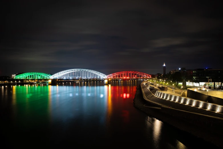 a bridge over a body of water at night, a tilt shift photo, by Oskar Lüthy, shutterstock, bauhaus, in empty!!!! legnica, red green black teal, tokujin yoshioka, colorful striped pavillions