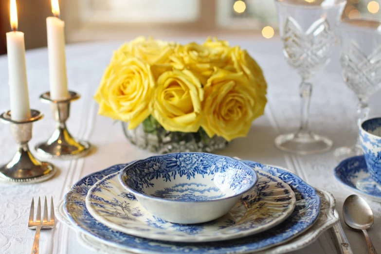 a white table topped with blue and white plates and silverware, a picture, by Joy Garnett, pixabay, rococo, yellow rose, bowl, yellow theme, 3 - piece