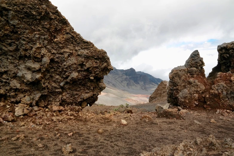 a couple of large rocks sitting on top of a dirt field, les nabis, horizon of an erupting volcano, looking into a mysterious cave, on a cloudy day, pov photo