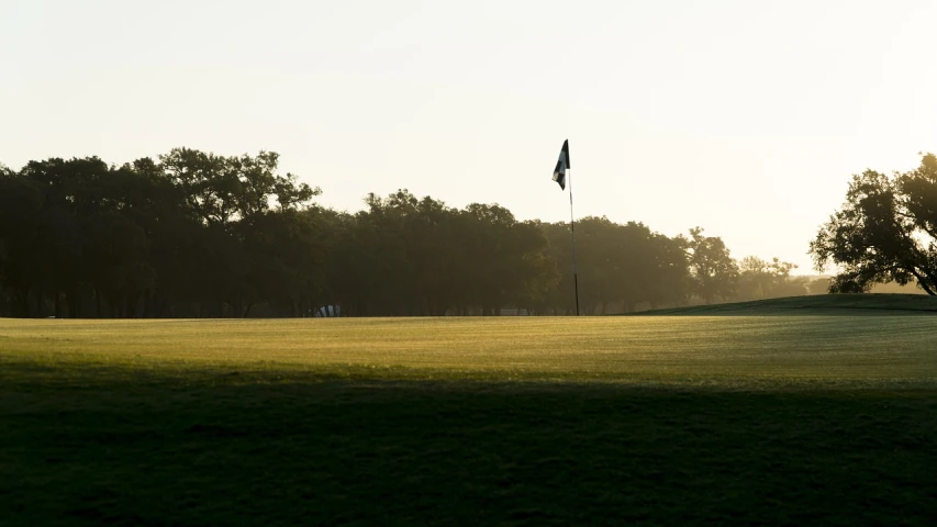 a man flying a kite on top of a lush green field, by Andrew Domachowski, augusta national, early morning, flag, oaks