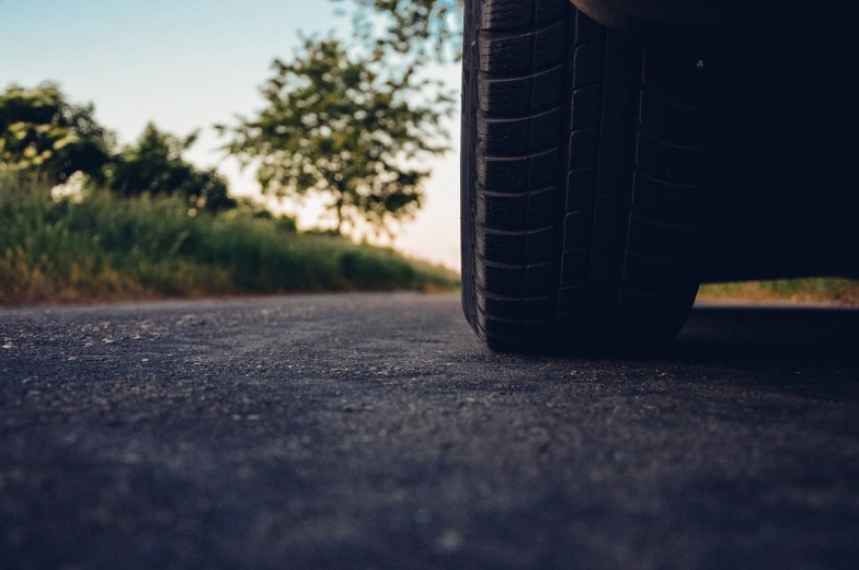 a close up of a tire on a road, a picture, by Thomas Häfner, unsplash, next to a tree, gentle shadowing, wallpaper mobile, full view of a car