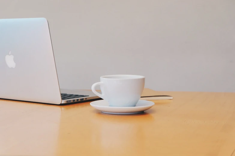 a laptop computer sitting on top of a wooden table, a portrait, minimalism, cup of death, set against a white background, office background, leaked image