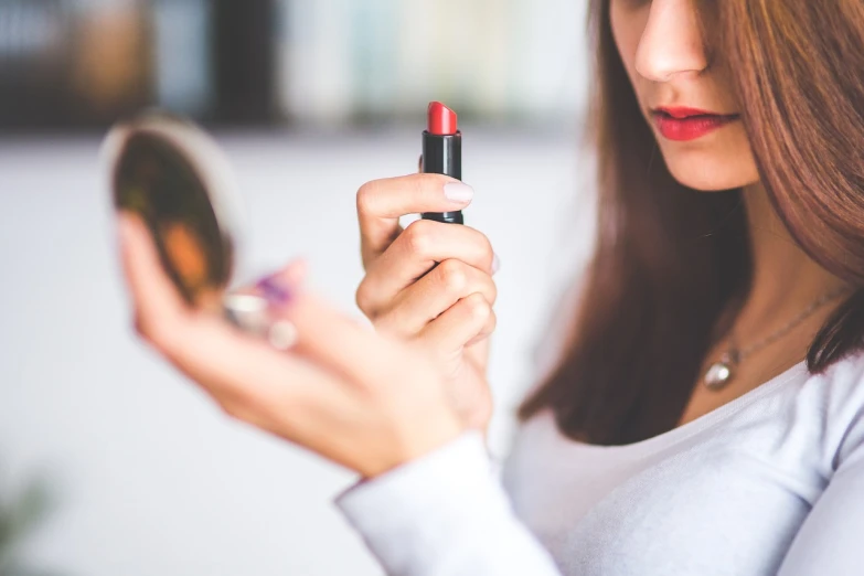 a woman holding a red lipstick in front of a mirror, a picture, shutterstock, tachisme, colour corrected, stock photo, girl with brown hair, istockphoto