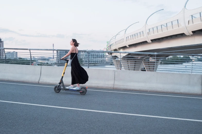 a woman riding a scooter on a bridge, happening, summer evening, boston dynamics, nice slight overcast weather, on the concrete ground