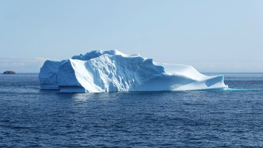 a large iceberg floating in the middle of the ocean, by Jørgen Nash, blue sky, seen from the side, istockphoto, cold blue light