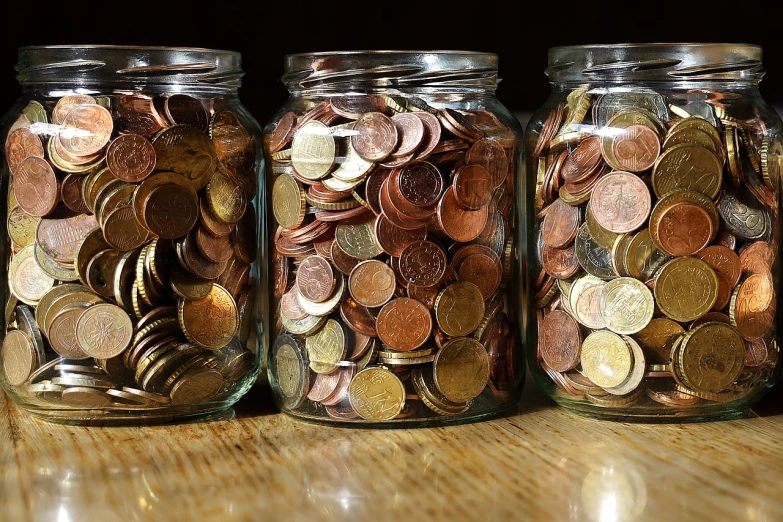 three jars filled with coins sitting on top of a wooden table, the photo shows a large, run, from the 7 0 s, cost