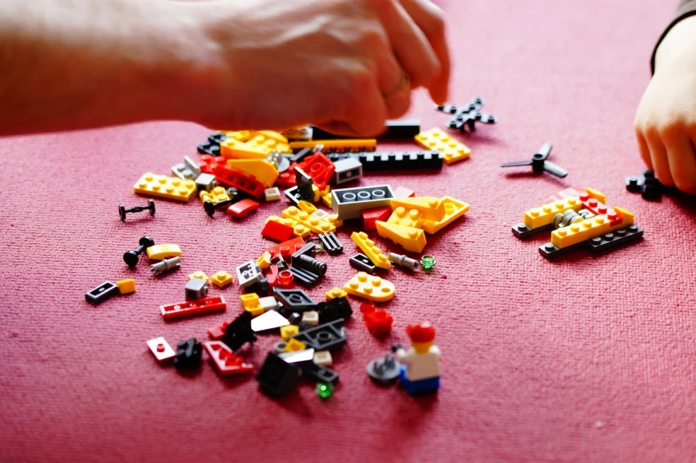 a person is playing with legos on a table, process art, high detailed photo, on a red background, spare parts, many pieces