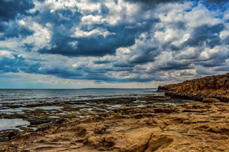 a large body of water sitting on top of a rocky beach, romanticism, magnificient clouds, agrigento, fotografia, cyprus