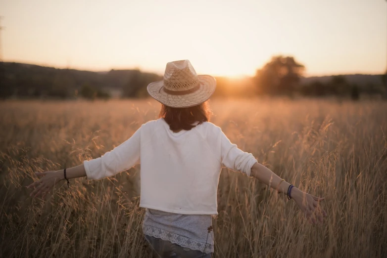 a woman standing in a field of tall grass, shutterstock, autumn sunrise warm light, with straw hat, walking away, wearing a white blouse