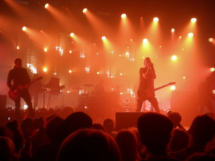 a group of people standing on top of a stage, a picture, singer songwriter nin, soft red lights, smokey lights, playing guitar onstage