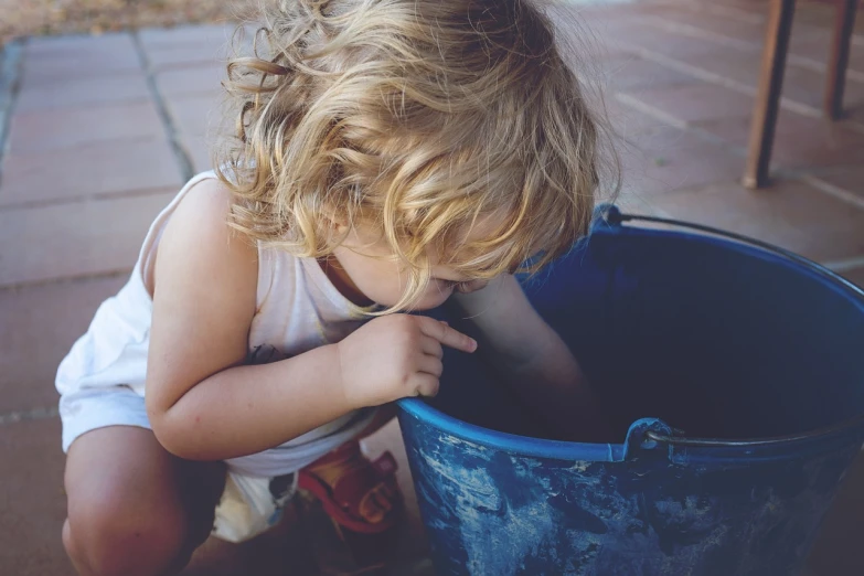 a small child playing with a blue bucket, a picture, pexels, messy blond hair, vintage color, dirty clothes, beautiful and cute