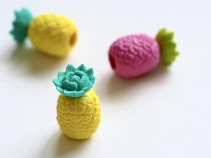 a close up of three toy pineapples on a white surface, inspired by Władysław Podkowiński, plasticine, turquoise pink and yellow, shot on 1 6 mm, bottle