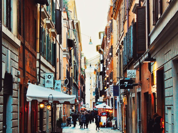 a group of people walking down a street next to tall buildings, by Antonio Rotta, shutterstock, digital art, old roman style, warm street lights store front, back alley, beautiful wallpaper