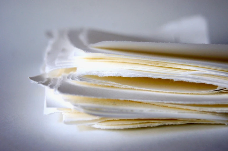a stack of papers sitting on top of a table, by Anita Kunz, flickr, rice paper texture, slice of life, soft glow, snowy