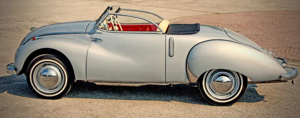 a vintage car parked on the side of the road, inspired by Bernardo Cavallino, trending on pixabay, purism, grey metal body, open top, scarab, wide body