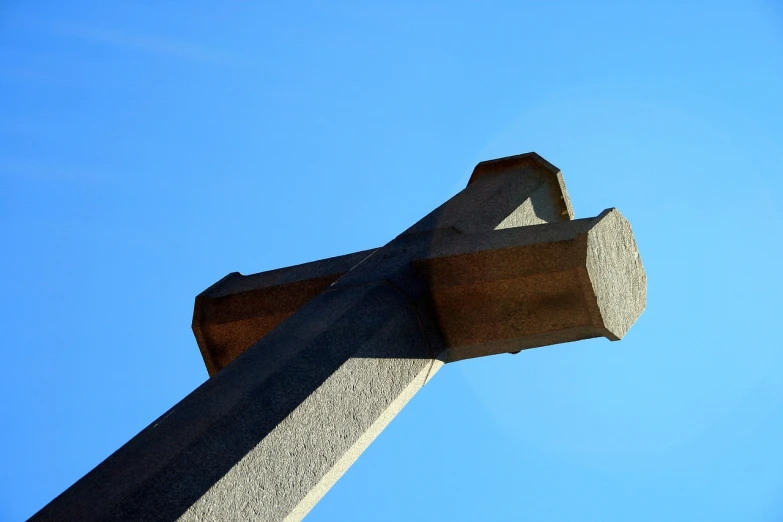 a cross with a blue sky in the background, an abstract sculpture, flickr, granite, beam, narrow angle, grain”