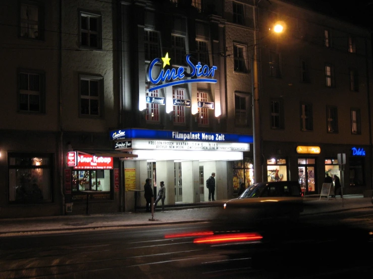 a car driving past a movie theater at night, a photo, by Werner Gutzeit, flickr, khedival opera house, stardust, entrance, torrent